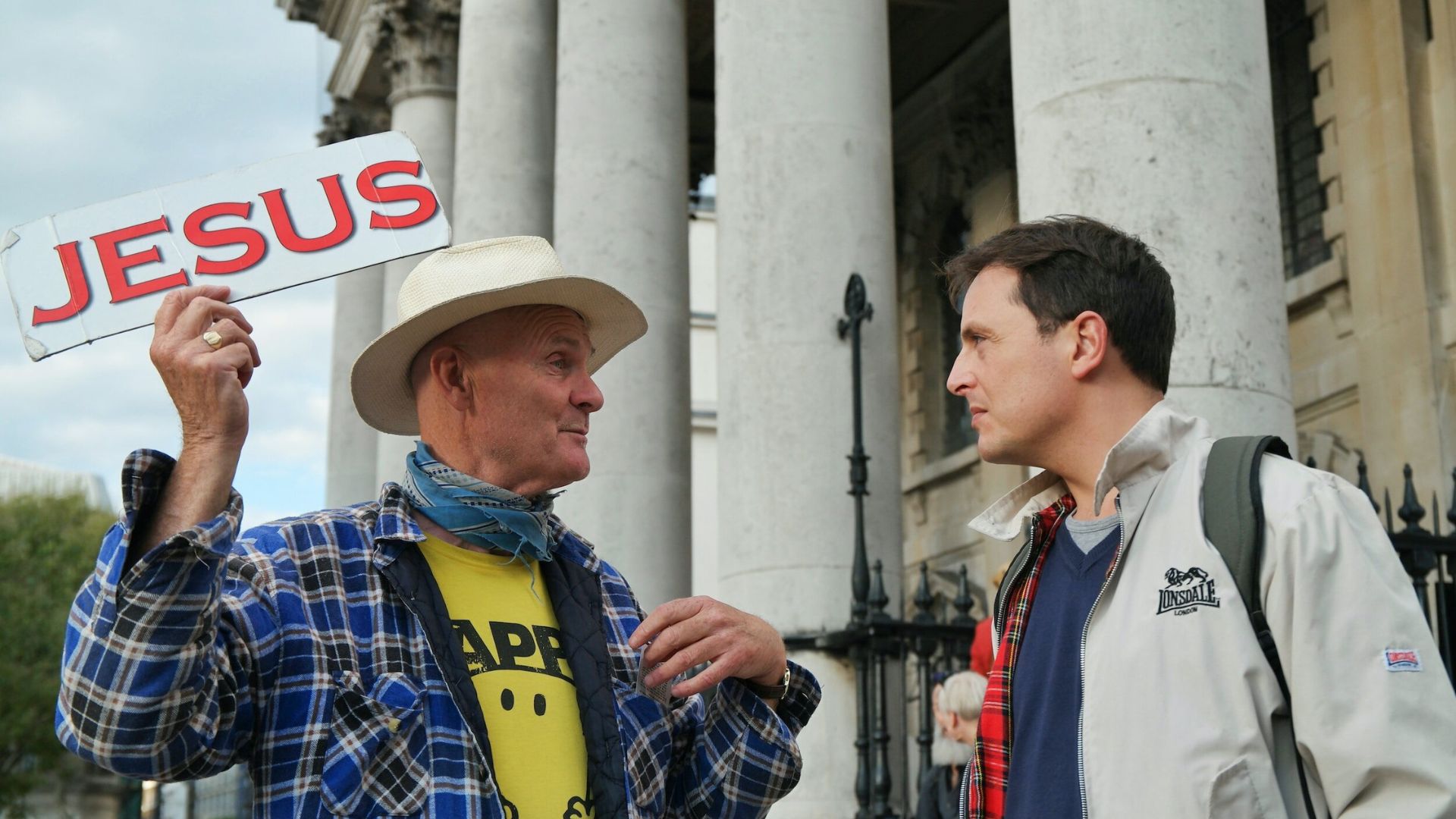 2 men talking about religious nones while the other one holding a card written JESUS